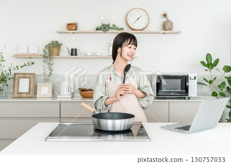 一位年輕的亞洲女性在廚房做飯時看著筆記型電腦 130757033