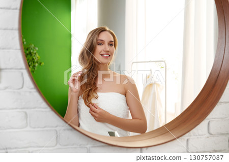 Woman getting ready in front of a circular mirror in a bright room with natural light and a green backdrop 130757087