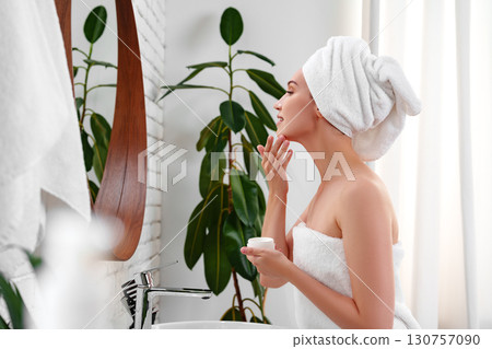 Woman applying facial cream in a serene bathroom setting with natural light during the day Woman applying facial cream in a serene bathroom setting with natural light during the day 130757090