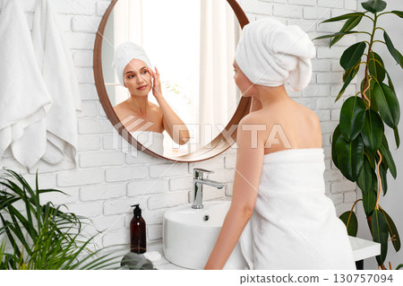 Woman applying skincare in bright bathroom with plants and modern decor during morning routine Woman applying skincare in bright bathroom with plants and modern decor during morning routine 130757094