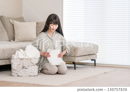 A young Asian woman folding laundry in the living room of her home (housekeeper, housekeeping service, maid) 130757839