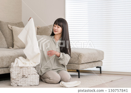 一位年輕的亞洲女性在家中客廳折疊衣物（家務、家庭主婦、全職家庭主婦） 130757841