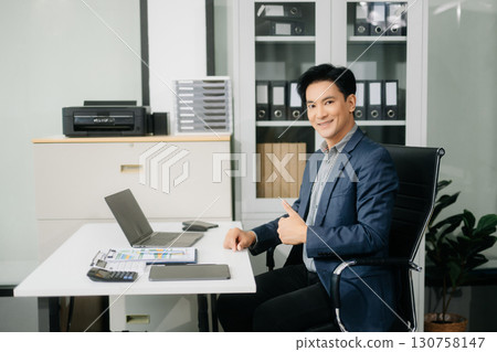 Handsome man typing on tablet and laptop while sitting at the working wooden table modern office 130758147