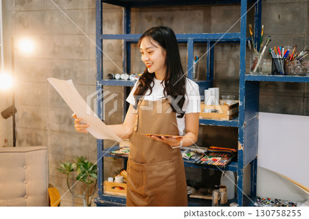 Cheerful female artist painting in a vibrant studio with brushes, a palette, and a blank canvas. Cheerful female artist painting in a vibrant studio with brushes, a palette, and a blank canvas. 130758255