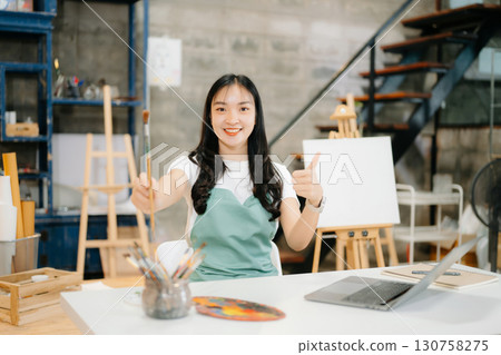 Cheerful female artist painting in a vibrant studio with brushes, a palette, and a blank canvas. Cheerful female artist painting in a vibrant studio with brushes, a palette, and a blank canvas. 130758275
