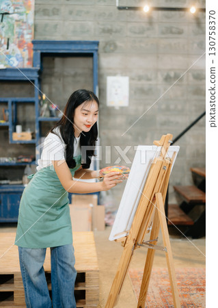 Cheerful female artist painting in a vibrant studio with brushes, a palette, and a blank canvas. Cheerful female artist painting in a vibrant studio with brushes, a palette, and a blank canvas. 130758370