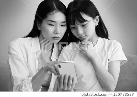 一位母親和女兒認真地看著智慧型手機的圖片 130758557