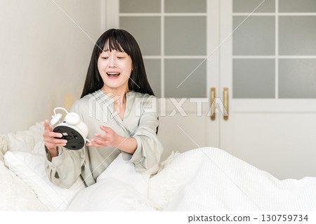年輕的亞洲女性看到鬧鐘時感到驚訝和驚訝（睡過頭、遲到、睡過頭） 130759734