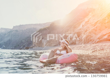 Woman, beach, summer. Happy young woman floats on a donut in the calm sea at a sunny pebble beach. 130759981
