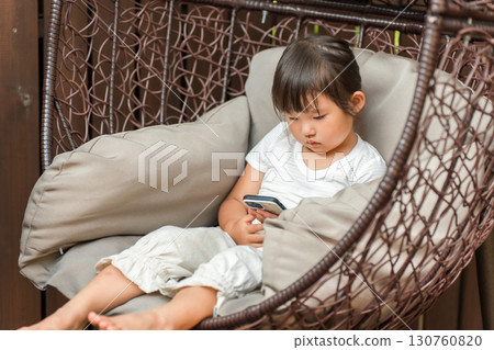 A girl sitting on a hanging chair and looking at her smartphone A girl sitting on a hanging chair and looking at her smartphone 130760820