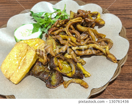 A plate of traditional Indonesian food, featuring fried chicken intestines, tofu, and fresh vegetables served on a unique woven plate. Ideal for authentic cuisine and travel concepts. 130761436