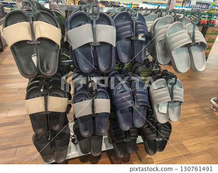 A retail display rack showing rows of various colors and styles of plastic slide sandals or slippers hanging for sale in a store. Ideal for fashion, retail, and footwear concepts. 130761491