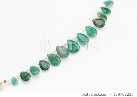 Emerald briolette bead strands and tassels against a white background 130762225