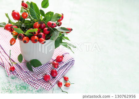 Fresh rose hips with green leaves overflowing a white cup Fresh rose hips with green leaves overflowing a white cup 130762956