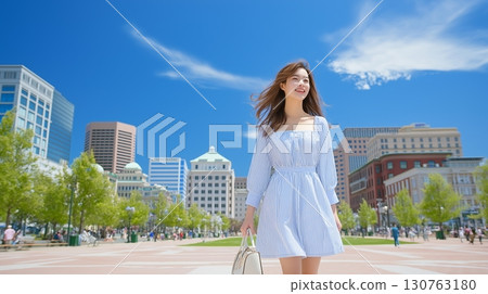 A woman walking in a city park under a blue sky 130763180
