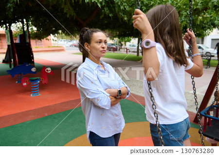 Mother Observing Her Daughter Playing at the Playground Swings 130763280