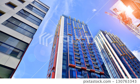 Exterior of a high modern multi-story apartment building - facade, windows and balconies. Timeless glass facade. Modern urban living district. 130763343