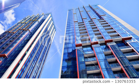 Exterior of a high modern multi-story apartment building - facade, windows and balconies. Timeless glass facade. Modern urban living district. 130763355