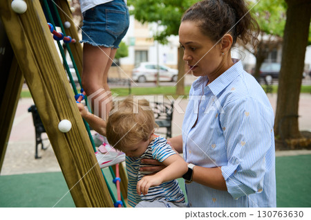 Mother Supporting Her Child on a Playground Adventure Outdoors 130763630