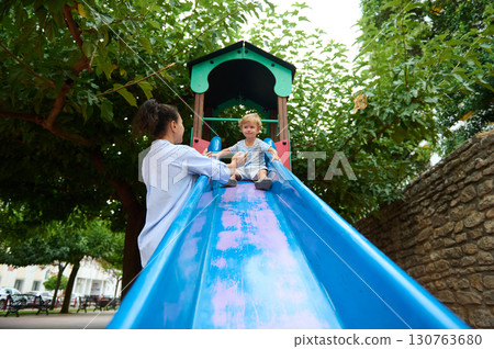 Parent and Child Playing at Colorful Park Slide on a Sunny Day 130763680