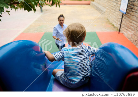 Child Playing on a Slide in Playground with Parent Watching Nearby Child Playing on a Slide in Playground with Parent Watching Nearby 130763689