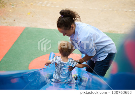 Mother Helping Child Slide on Playground for Fun and Adventure Mother Helping Child Slide on Playground for Fun and Adventure 130763693