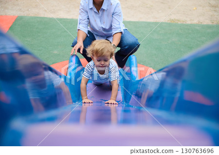 Child Climbing a Slide with Parental Support at Outdoor Playground 130763696