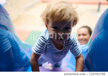 Child Climbing a Playground Slide While Smiling and Mother Observing 130763700