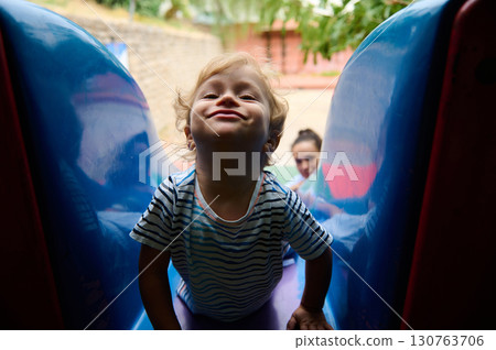 Child Playing on a Slide at an Outdoor Playground 130763706