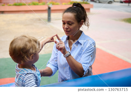 Mother Teaching Child Through Gestures Outdoors on a Bright Day 130763715