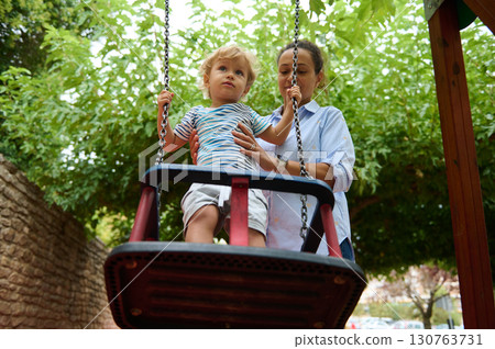Mother and Child on a Swing in a Sunny Park Setting Mother and Child on a Swing in a Sunny Park Setting 130763731