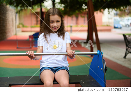 Smiling Girl Playing on Seesaw in a Colorful Playground Outdoors 130763917