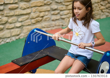 Young Girl Playing on a Teeter-Totter in a Playground Setting Young Girl Playing on a Teeter-Totter in a Playground Setting 130763918