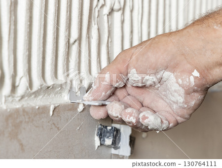 Craftsman hand place tile spacers during tiling a wall, closeup. Construction or rennovation of a house Craftsman hand place tile spacers during tiling a wall, closeup. Construction or rennovation of a house 130764111