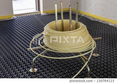Roll with pipes placed over black insulation sheets. Underfloor heating system in a new building 130764113