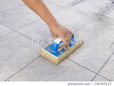 Craftsman washing ceramic tiles with a sponge float during construction of a building, hand closeup 130764115