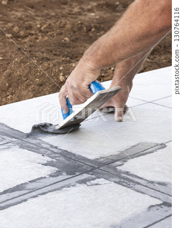 Craftsman filling tile joints with grout using a float, hand closeup, building construction detail 130764116