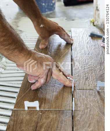 Craftsman places ceramic tile on a house floor, hands closeup. Building construction or rennovation 130764124