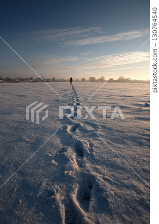 Footprints in fresh snow leading to a tiny Santa silhouette on horizon 130764540