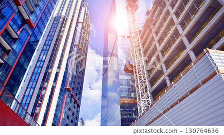 Crane on the construction site in a site surrounded by the high buildings. Office building under construction in the vicinity of high apartment buildings and office building. 130764636