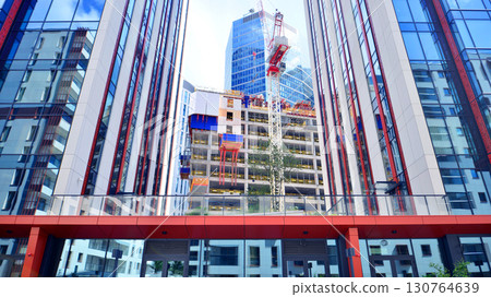Crane on the construction site in a site surrounded by the high buildings. Office building under construction in the vicinity of high apartment buildings and office building. 130764639