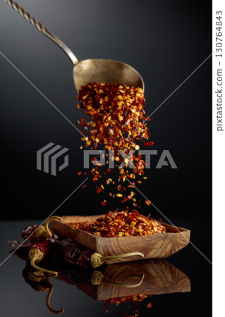 Dry red chili peppers and crushed chili flakes on a black reflective background. Dry red chili peppers and crushed chili flakes on a black reflective background. 130764843