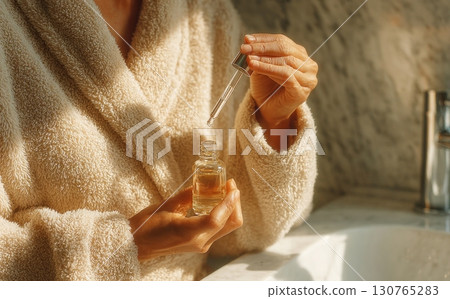 Woman wearing bathrobe using cosmetic serum in bathroom Woman wearing bathrobe using cosmetic serum in bathroom 130765283