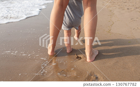 Mother helping baby take first steps on beach 130767782