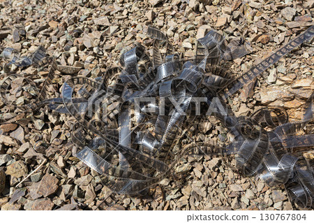 Discarded film strip lies tangled on gravel, representing lost memories or forgotten stories 130767804