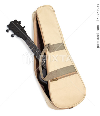 Black ukulele partially inside beige case on white background 130767935