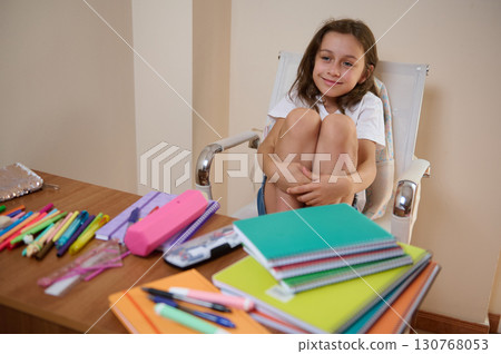 Young Girl Sitting Happily at Desk with Colorful Stationery and Notebooks Young Girl Sitting Happily at Desk with Colorful Stationery and Notebooks 130768053