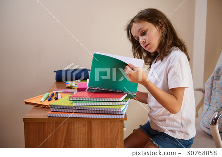 Young Girl Studying at a Desk with Notebooks and Supplies Young Girl Studying at a Desk with Notebooks and Supplies 130768058