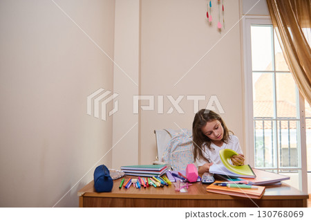 Young Girl Concentrating on Homework at a Desk With School Supplies 130768069