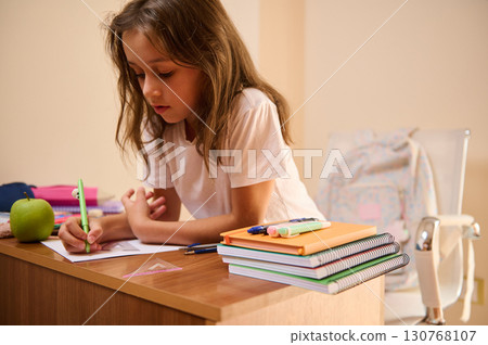 Young Girl Focused on Homework at Desk with School Supplies 130768107